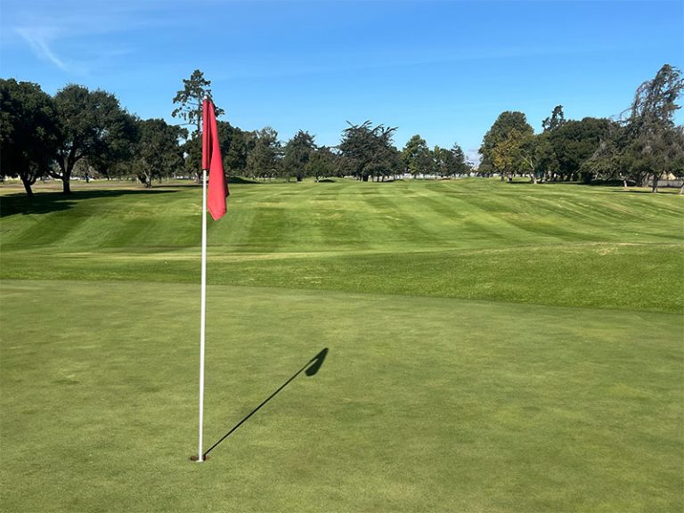 Red flag on a putting green overlooking a wide, striped fairway at Salinas Fairways Golf Course.