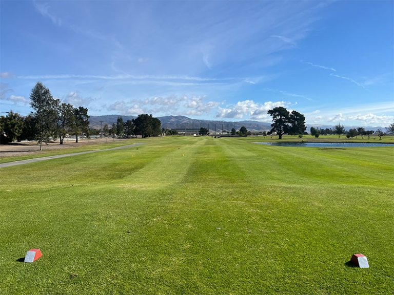 Wide fairway view from the tee box with mountains and a pond at Salinas Fairways Golf Course.